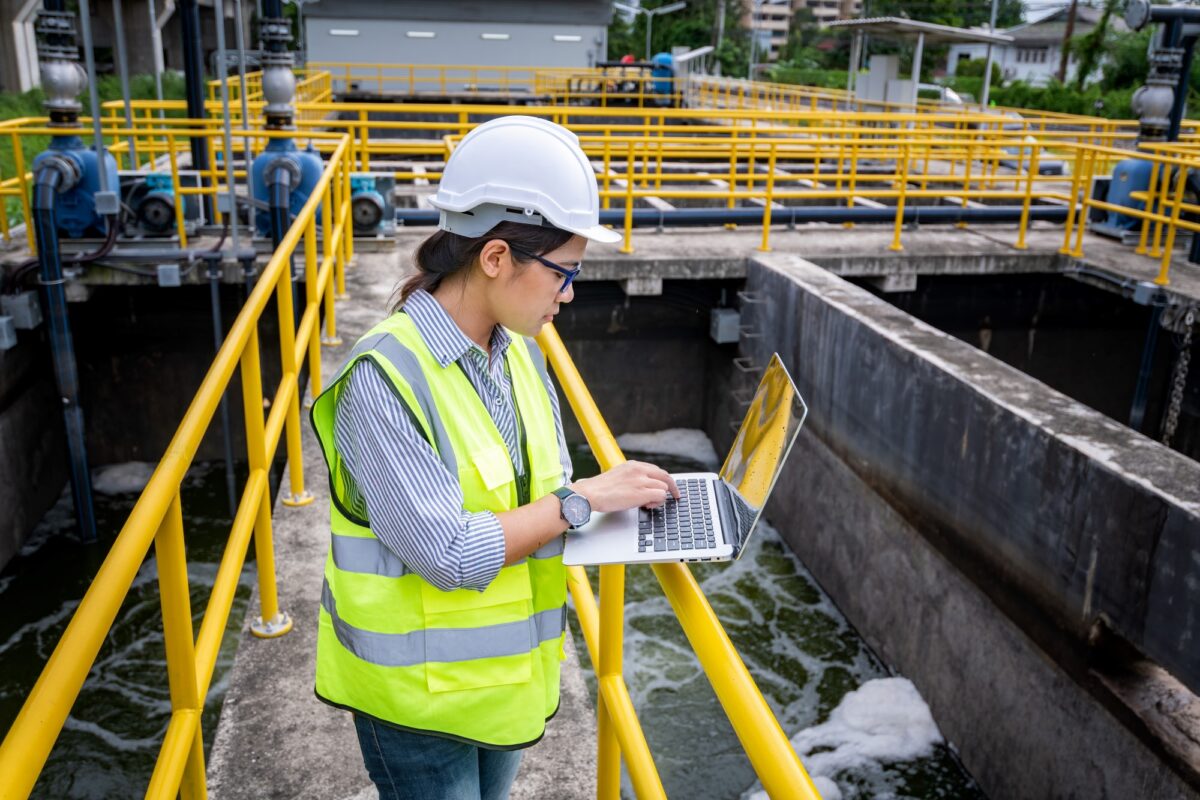 Technikerin mit Laptop auf Brücke im Klärwerk