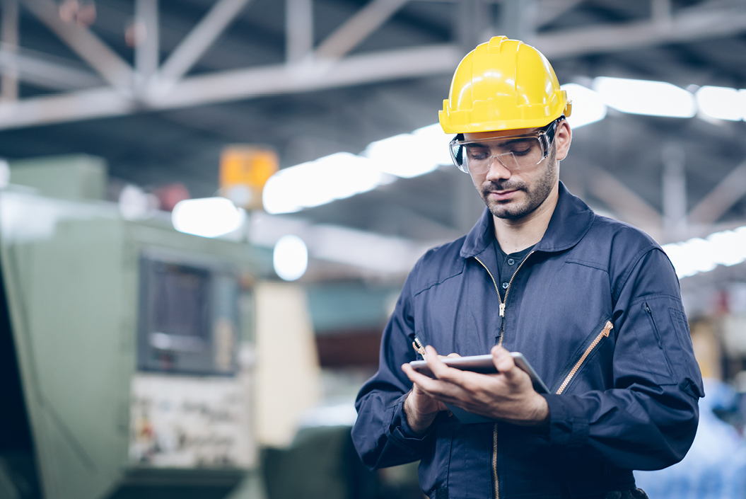 Techniker in Werkshalle mit Helm und Tablet